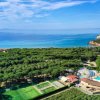 Vista dall'alto di una costa con vegetazione, piscine e mare azzurro.