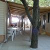 Area esterna di case mobili con sedie e tavolo sotto un pergolato, albero centrale.