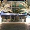 Ingresso di un hotel illuminato di sera, con palme e tavolini.