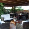 Un salotto esterno con mobili in vimini sotto una tettoia, decorato con piante.