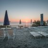 Spiaggia con lettini e ombrelloni chiusi, il mare al tramonto.