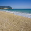 Spiaggia sabbiosa con mare blu e colline.