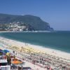 Spiaggia con ombrelloni colorati e un paese collinare sullo sfondo.