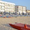 Spiaggia con ombrelloni chiusi e un pattino rosso.