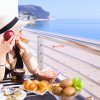 Donna con cappello fa colazione su terrazza vista mare.