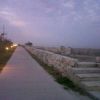 Una strada pedonale al tramonto con lampioni accesi e un muretto di pietra sulla destra.