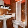 Bagno con piastrelle marroni, lavabo bianco, bidet, doccia chiusa e asciugamani arrotolati.