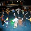 Bambini in cerchio, mascherati, danzano su un palco all'aperto illuminato.