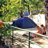 Tenda da campeggio blu su un terreno alberato, con due persone sedute vicine.