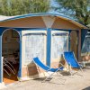 Camper con veranda e lettini su un piazzale vicino al mare.